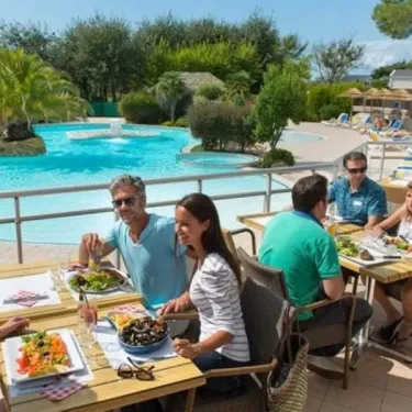 Des visiteurs dégustent un repas en plein air près de la piscine du camping Les Iles.