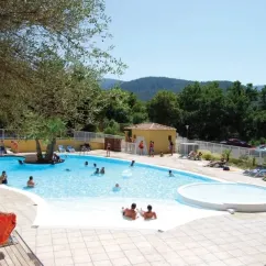 Camping Le Galoubet : piscine extérieure entourée d'arbres et de chaises longues sous un ciel bleu.