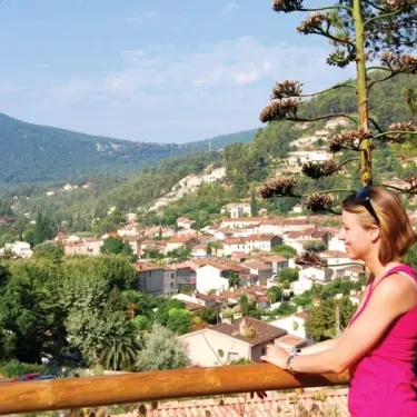 Un couple admire la vue sur le village depuis un balcon du Camping Le Galoubet, entouré de collines verdoyantes.