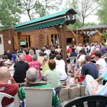 Camping Les Bonnets : groupe de personnes assises en plein air devant une cabane en bois.