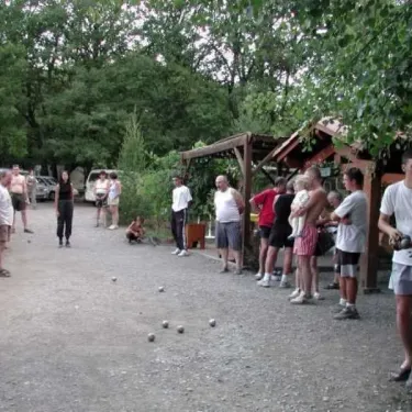 Camping Les Bonnets : groupe jouant au boule sur un chemin en gravier entouré d'arbres.