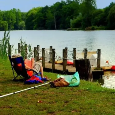 Un camping au lac avec un visiteur assis dans une chaise pliante près d'un quai en bois.