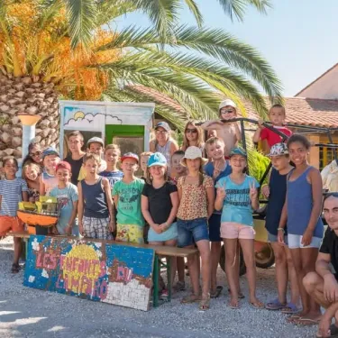 Groupe d'enfants et adultes souriants devant une cabane décorée au Camping Le Lamparo