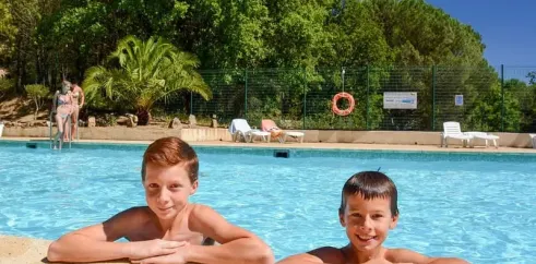 Deux enfants souriants à la bordure de la piscine dans un camping verdoyant
