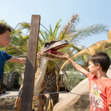 Enfants devant dinosaures en sculpture dans le parc du camping