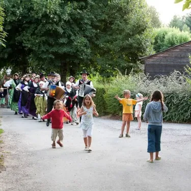 Enfants qui courrent devant une troupe traditionnelle au Camping Hameau Saint Martial