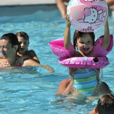 Enfant dans une piscine avec un ballon Hello Kitty et des flottants roses à Camping Les Ondines