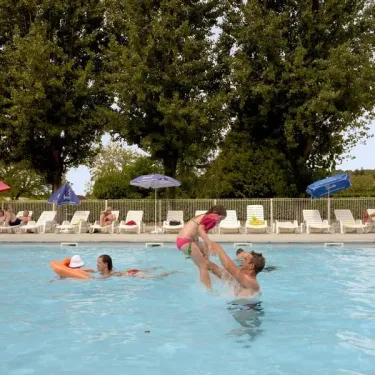 Un homme lance une petite fille dans la piscine à Camping Les Ondines
