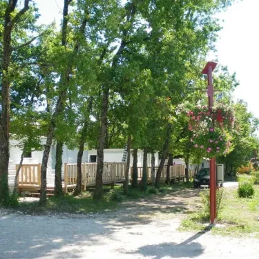Village de caravanes blanches entourées d'arbres, avec poteau décoratif fleuri au Camping Le Pontis.