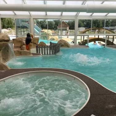 Piscine intérieure avec jacuzzi et cascade naturelle au Camping Domaine De La Roselière.
