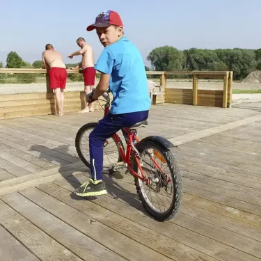 Enfant à vélo sur une passerelle en bois au Camping Domaine De La Roselière