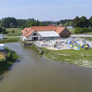 Vue aériale du camping avec piscine, espace jeux et lac bordant le site.