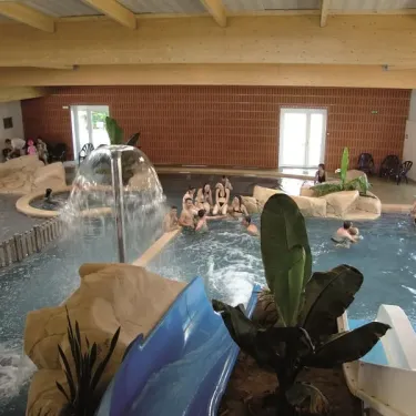 Piscine intérieure avec chutes d’eau et toboggan bleu au Camping La Boutinardière