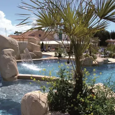 Piscine entourée de rochers et de palmiers au Camping La Boutinardière