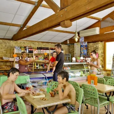 Clients au comptoir de la boutique du Camping Des Chênes Verts, avec des produits et des boissons.
