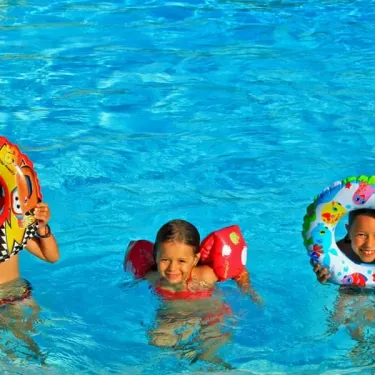 Enfants souriants dans une piscine avec flottants colorés au Camping Des Chênes Verts.