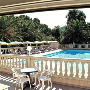 Terrasse avec parasols, chaises longues et piscine entourée de palmiers, Camping Résidence Thalassa