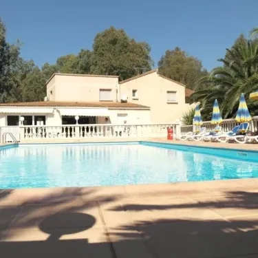 Piscine entourée de chaises longues blanches et d'un parasol bleu au Camping Résidence Thalassa
