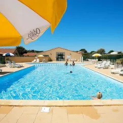 Piscine bleue avec parasol Odalys et chaises longues près d'un bâtiment au Camping Saint Martin