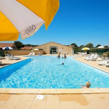 Piscine bleue avec parasol Odalys et chaises longues près d'un bâtiment au Camping Saint Martin