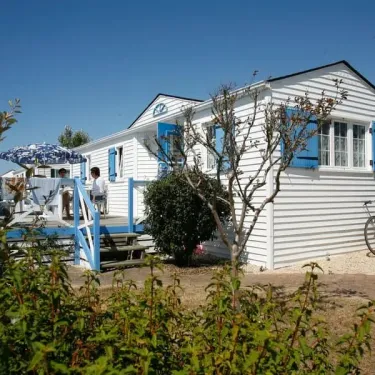 Camping Saint Martin : mobil-home blanc avec volets bleus, balcon, parasol et vélos à l'extérieur.