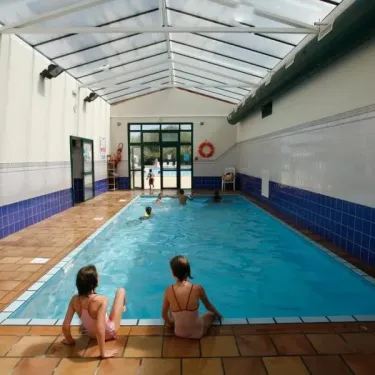 Piscine intérieure couverte avec enfants nageant et deux filles assises sur le bord au Camping Saint Martin