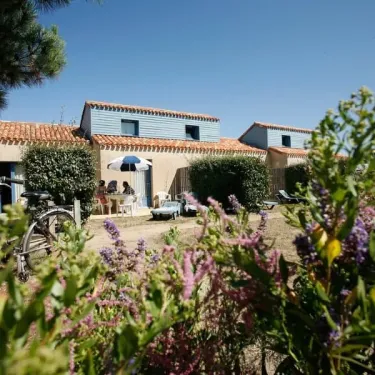 Camping Saint Martin : mobil-home bleu avec toit en tuiles, jardin fleuri et vélo devant.