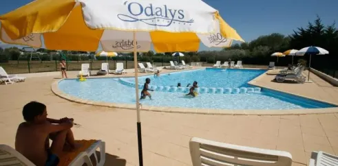 Enfants dans la piscine avec parasol Odalys et chaises longues autour du Camping Saint Martin