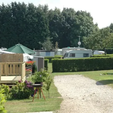 Village de caravanes verdoyant avec allées en gravier, jardin fleuri et cabanes, Camping Etennemare.