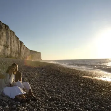 Couple assis sur une plage de galets à côté d'une falaise, soleil couchant sur l'océan, Camping Etennemare.