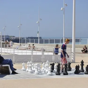Deux personnes jouent aux échecs géants sur une promenade en bord de mer, Camping Etennemare.