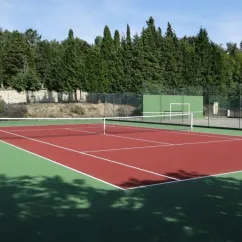 Terrain de tennis rouge entouré d'arbres, Camping Lé Moulis