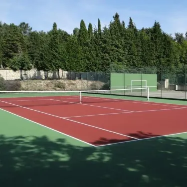 Terrain de tennis rouge entouré d'arbres, Camping Lé Moulis