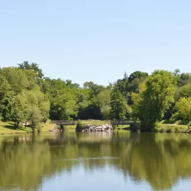 Piscine entourée d'arbres et d'un pont en pierre au Camping Le Bosquet 12.