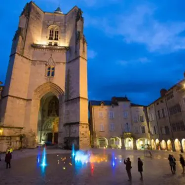 Place animée avec une église illuminée au crépuscule, Camping Le Bosquet 12 à proximité
