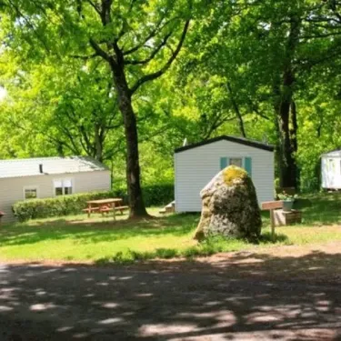 Camping Le Bosquet 12 : mobil-homes en forêt, table de pique-nique et rocher couvert de mousse.