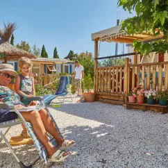 Une femme et un enfant relaxent sur des chaises longues devant une cabane en bois au Camping Ensoya.