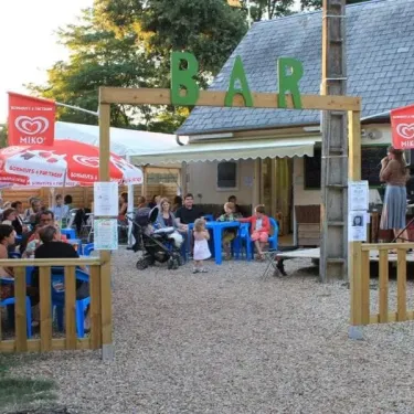 Bar extérieur du camping Les Acacias - 37 avec des clients assis sous des parasols Miko.