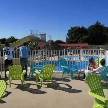 Piscine avec toboggan, chaises vertes et visiteurs près du bord au Camping Le Parc de la Grève