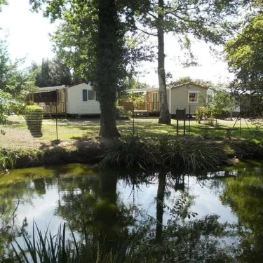 Camping Le Parc de la Grève : mobile homes entourés d'arbres près d'un étang.
