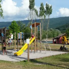 Camping du Lac de Moselotte : aire de jeux pour enfants avec toboggan jaune et structures en bois.