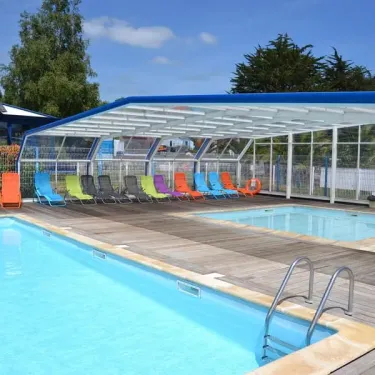 Piscine couverte avec chaises longues colorées au Camping La Mer Blanche