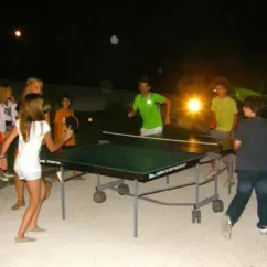 Enfants jouent au ping-pong la nuit au Camping Quercy Vacances sous les lampadaires.