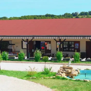 Bâtiment principal du Camping Quercy Vacances avec toit rouge et jardin fleuri.
