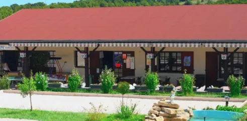 Bâtiment principal du Camping Quercy Vacances avec toit rouge et jardin fleuri.
