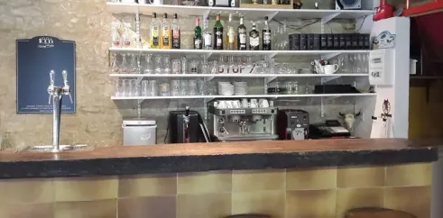 Bar avec étagères de boissons, cafetière et tabourets au Camping Les Rives du Céou