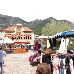 Marché animé devant la mairie de Camping Les Templiers, avec des stands et des montagnes en arrière-plan.