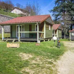 Cabines de Camping Le Grangeon avec balcon et vélo près d'un mur de pierre