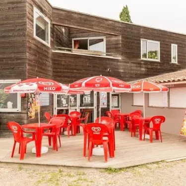 Terrasse extérieure avec tables et chaises rouges sous parasols Miko au Camping le Beauchêne