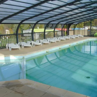 Piscine couverte avec chaises longues blanches et une chaise verte, Camping le Beauchêne